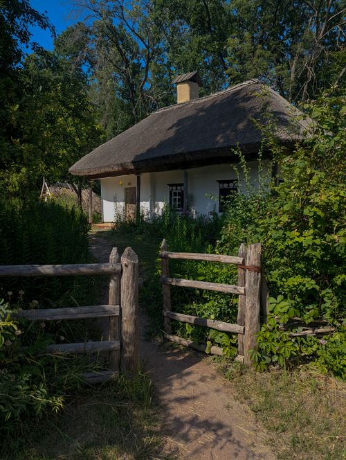 Free Picturesque thatched roof cottage surrounded by lush greenery and rustic wooden fence. Stock Photo