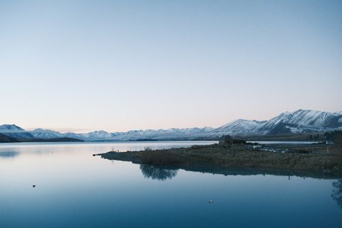 Free A serene view of Lake Tekapo at twilight with snow-capped mountains in New Zealand. Stock Photo