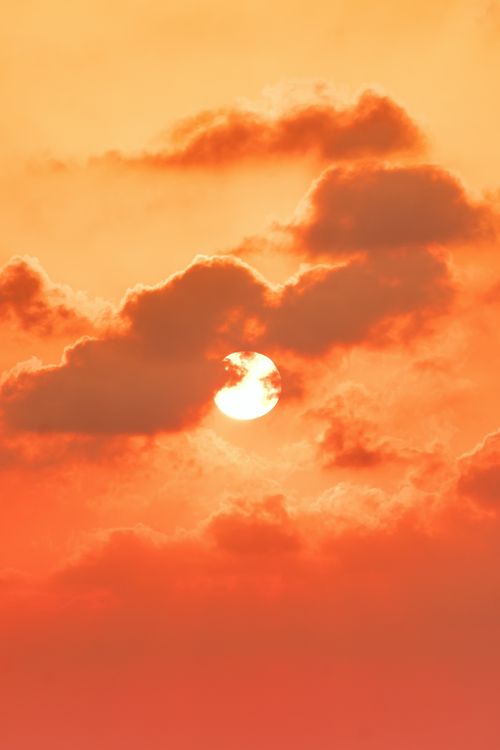 Free Vivid sunset with clouds partially covering the sun, casting a dramatic orange hue. Stock Photo