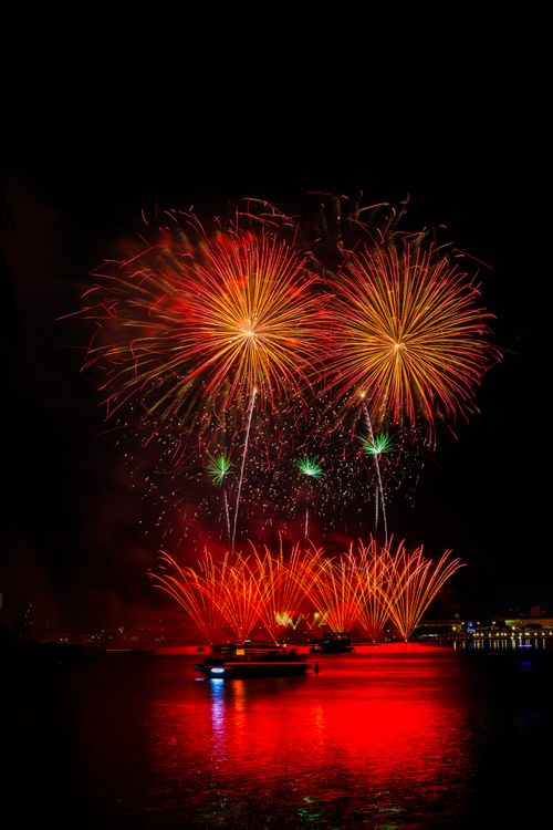 Free Vivid fireworks lighting up the night sky over a water body. Stock Photo