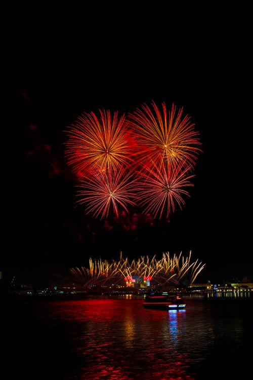 Free Red fireworks illuminate the night sky over water, reflecting vibrant hues. Stock Photo