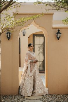 A bride in elaborate traditional attire poses outdoors under an arched doorway, showcasing cultural elegance.