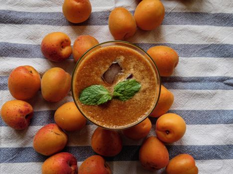 Top view of a refreshing apricot smoothie with mint leaves, surrounded by fresh apricots on a striped cloth.
