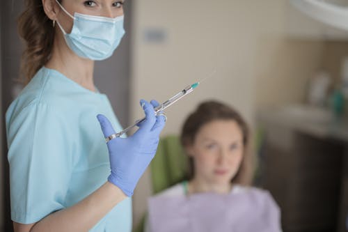 Young female dentist holding syringe in hand while working with patient in clinic