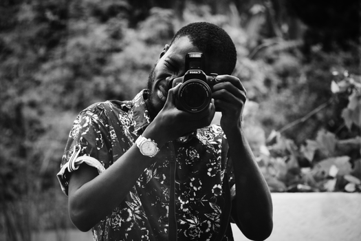 Black and white image of a young male photographer taking a picture with a DSLR camera.