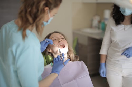 Young female dentist in latex gloves and mask doing injection while treating teeth of patient during work in modern clinic