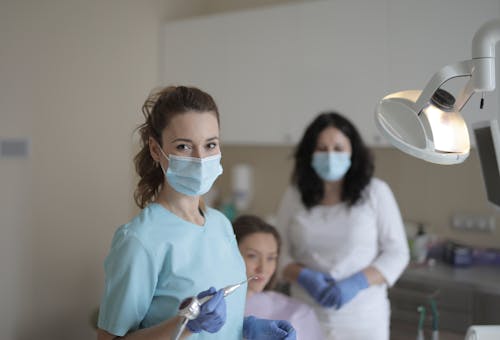 Female dentists treating teeth of patient in modern clinic