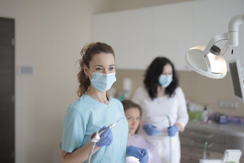 Free Young female dentist working with assistant while treating patient in modern hospital Stock Photo