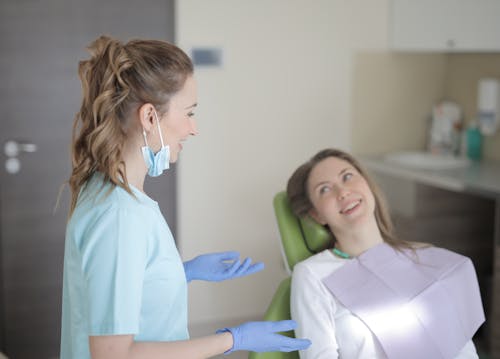 Cheerful young female dentist talking with patient during therapy in modern hospital