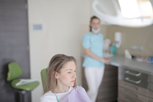 Thoughtful young female patient sitting in dental chair and waiting for treatment while looking away in modern dental room in hospital
