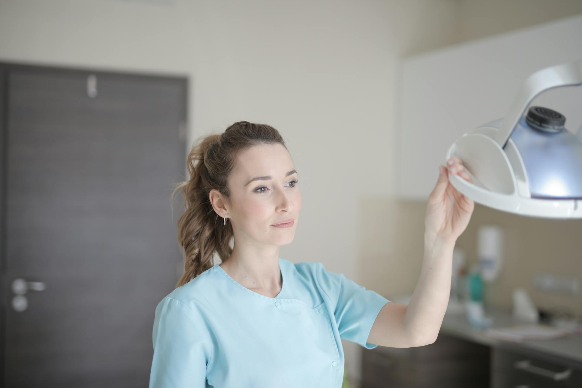 Confident female medical professional adjusting examination light in a clinic setting, showcasing care and precision.