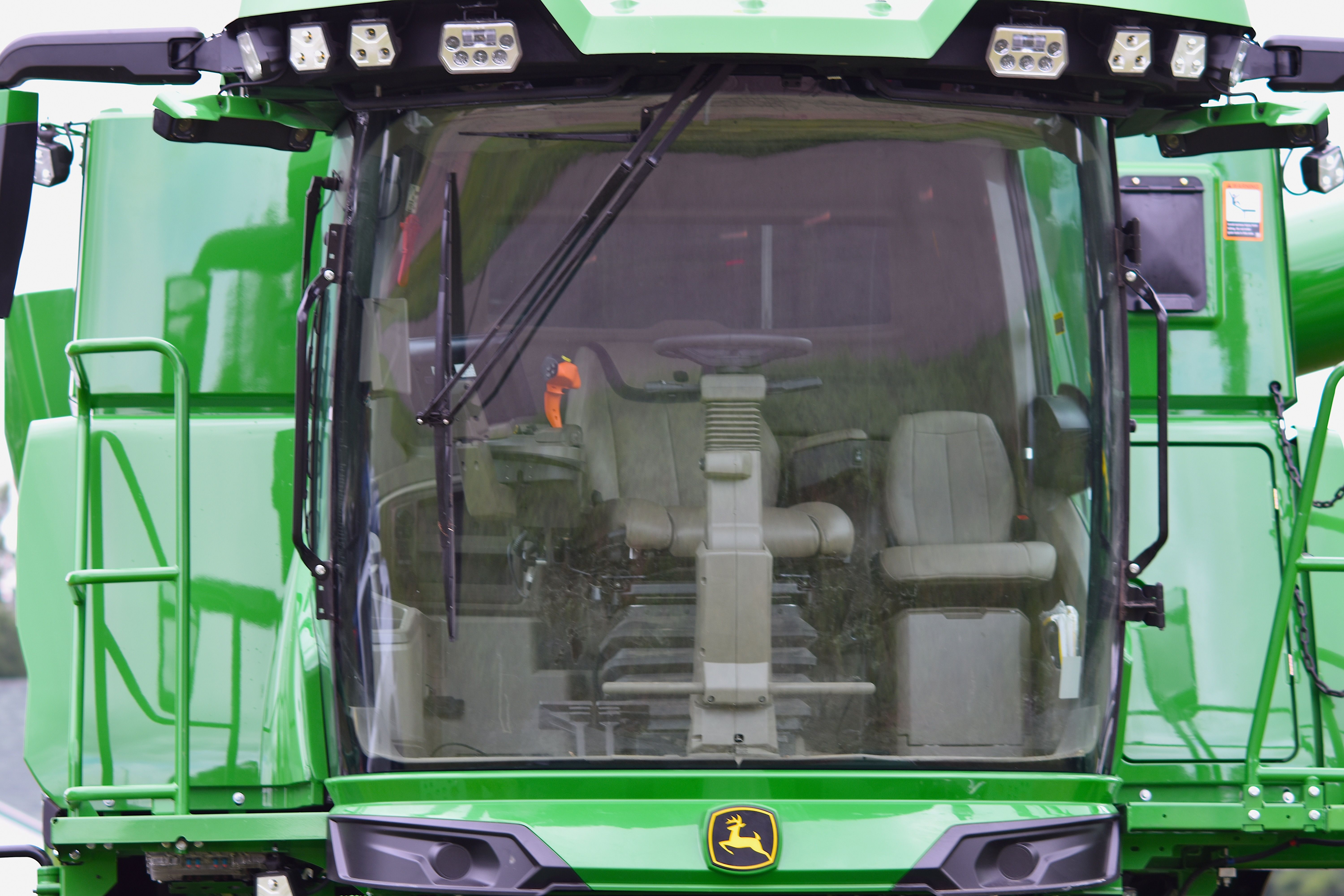Detailed view of a green tractor cab with a clear windshield, showcasing modern farm equipment.