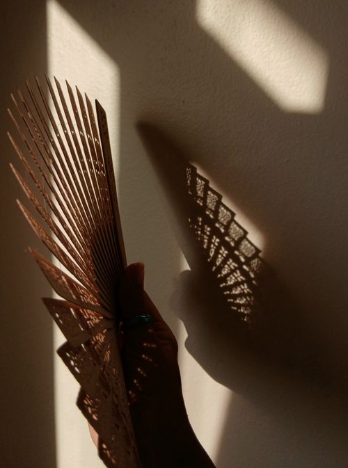 Free A handheld fan casting intricate shadows on a wall in soft light, creating a dramatic effect. Stock Photo