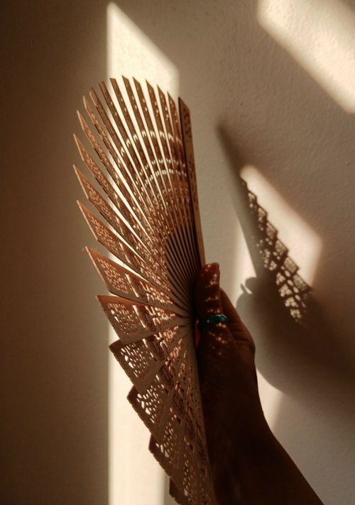 Free A hand holds an intricately carved wooden fan casting artistic shadows on a wall. Stock Photo