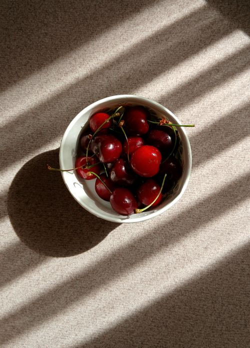 Free Fresh ripe cherries in a white bowl, highlighted by dramatic sunlight through blinds. Stock Photo