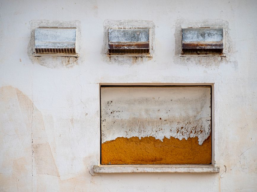 Rust-stained wall with heavy iron oxide bleed below vents, showing water-driven corrosion damage on a Mediterranean faca