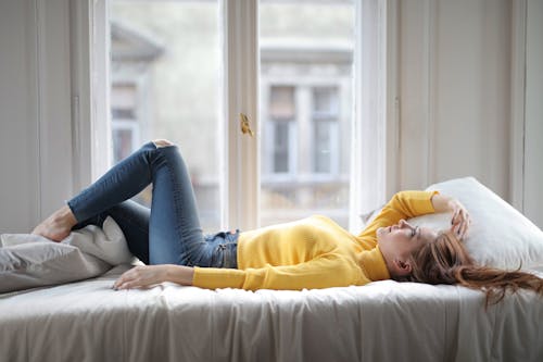 Relaxed young lady resting on bed near window in light bedroom