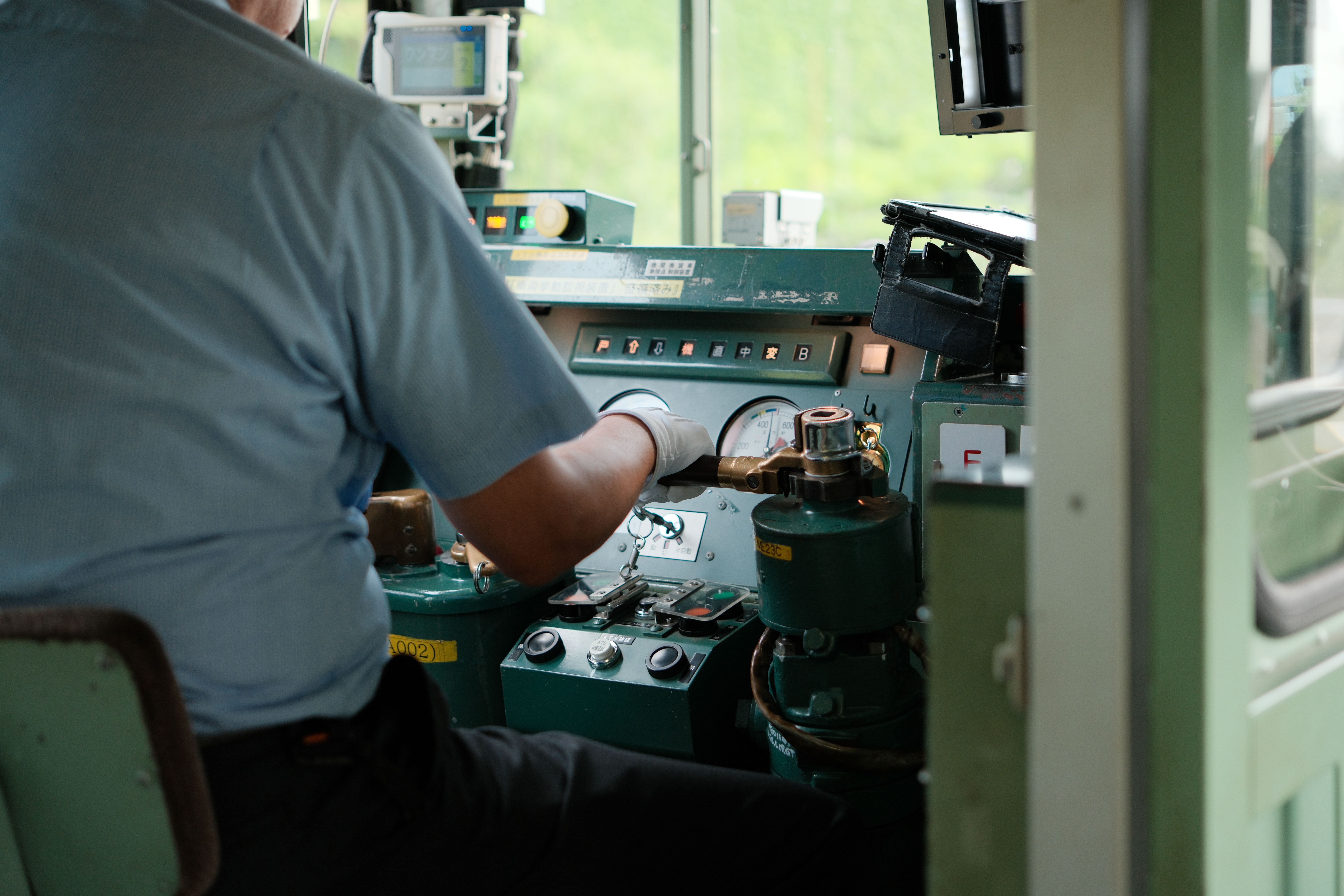 A train conductor operates controls in a Japanese train cabin. Close-up of instruments and gauges.