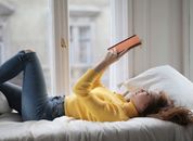 Young peaceful woman reading book on bed