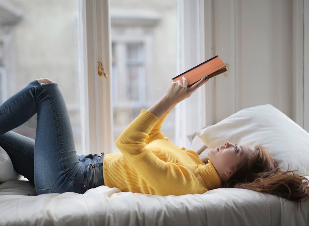 Free Young peaceful woman reading book on bed Stock Photo