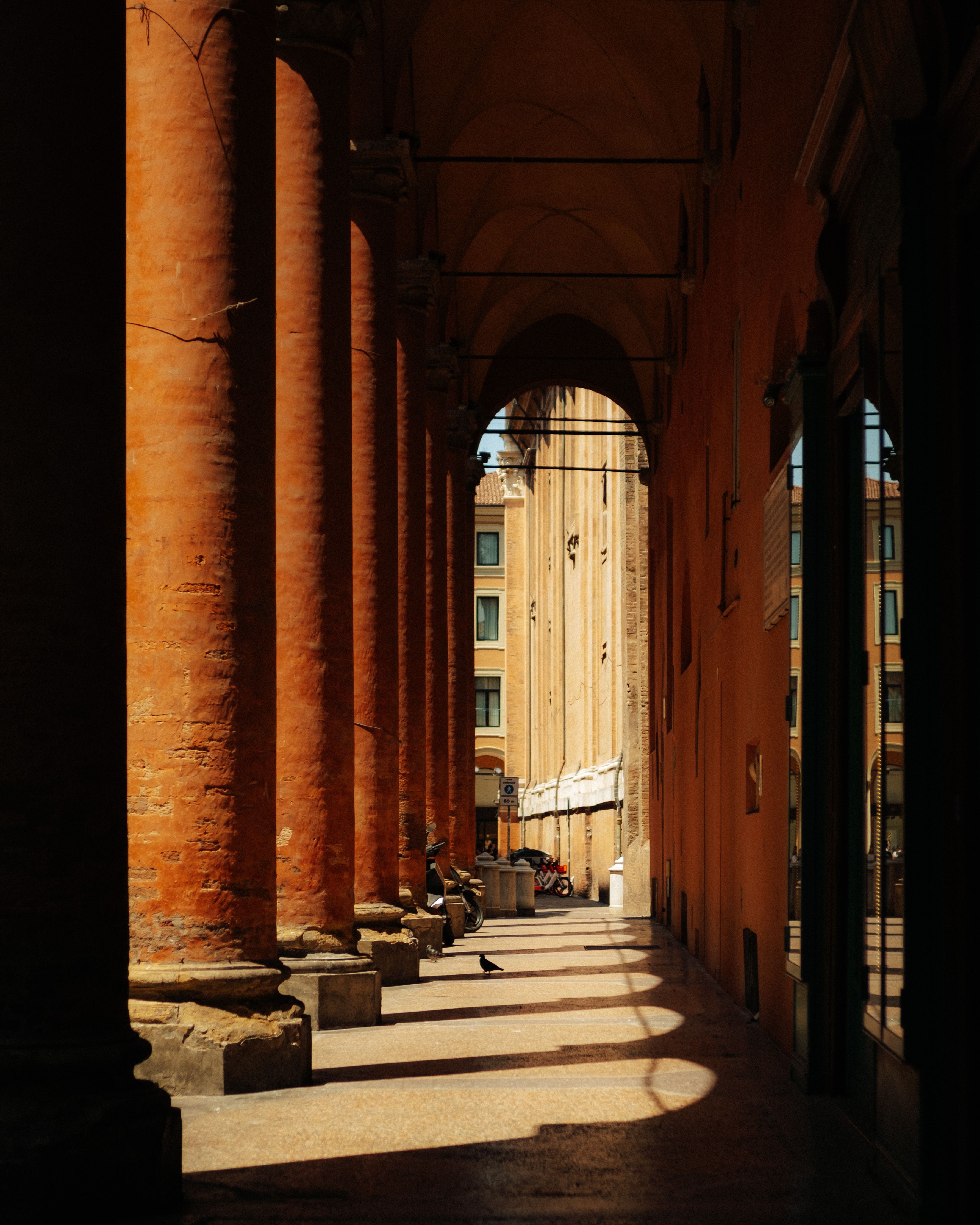 A sunlit portico in Bologna, Italy with classic architecture and shadows.