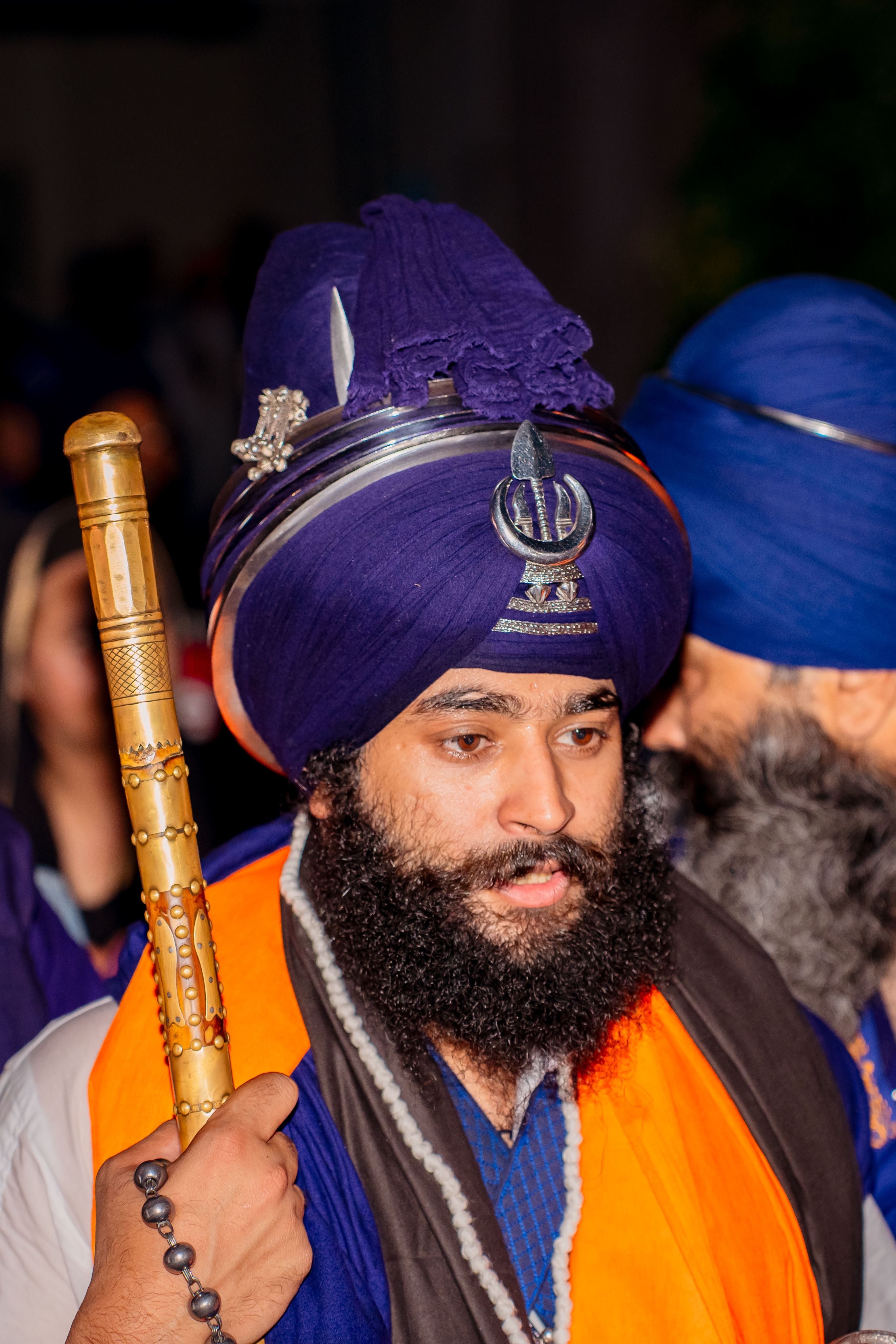 Sikh man in traditional attire holding a ceremonial staff at a cultural event.