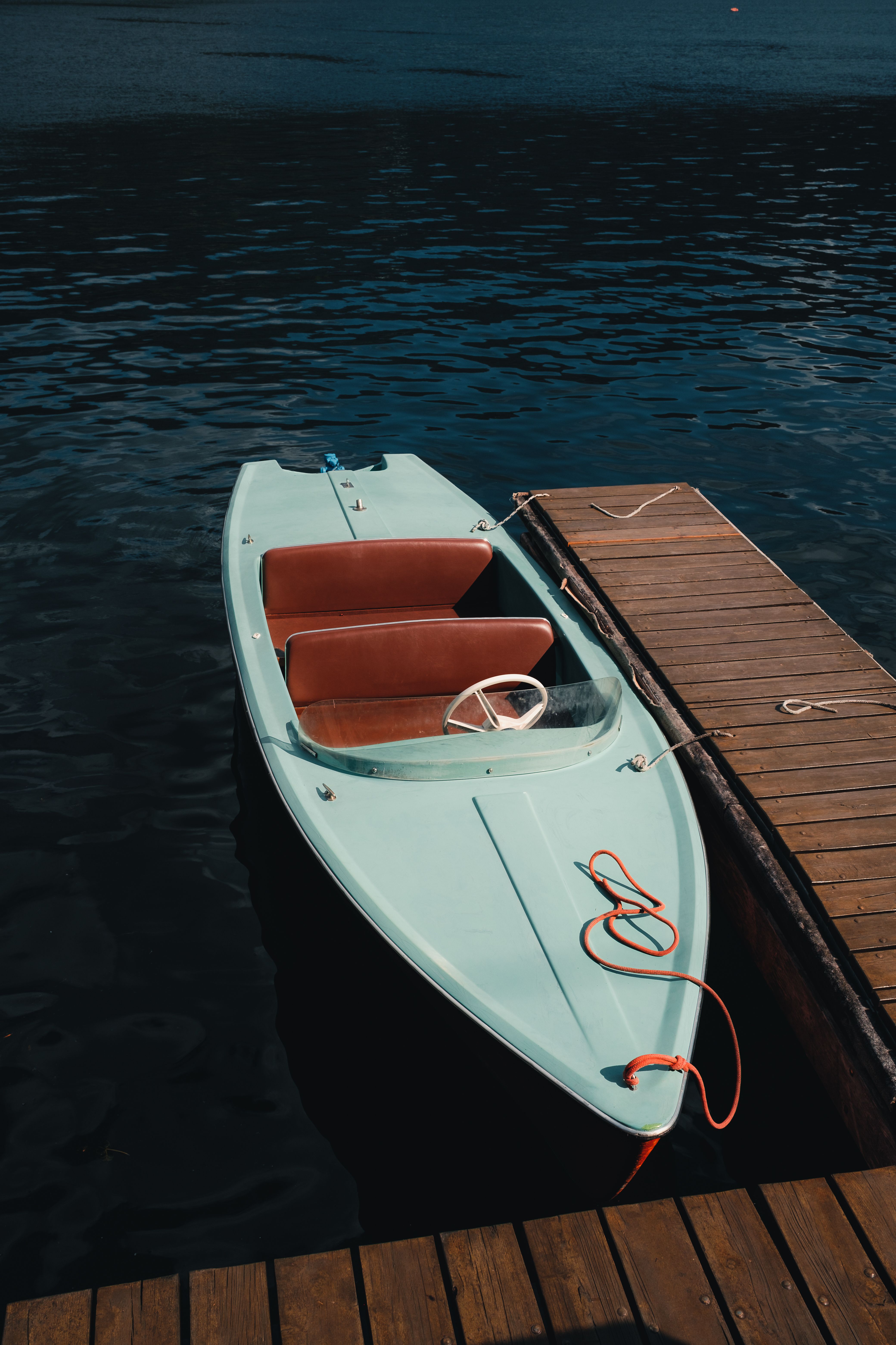 A vintage speedboat tied to a wooden dock on a serene Austrian lake under a bright sky.