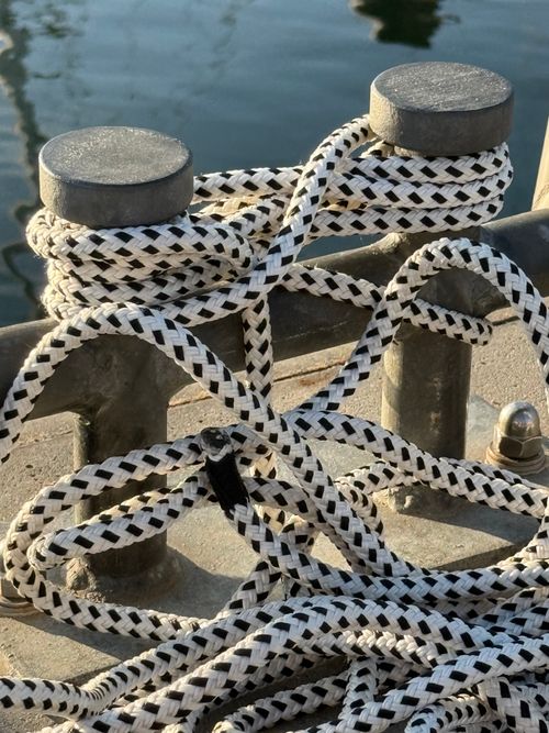 Free Close-up of nautical ropes tied intricately around a metal bollard on a sunny day by the water. Stock Photo
