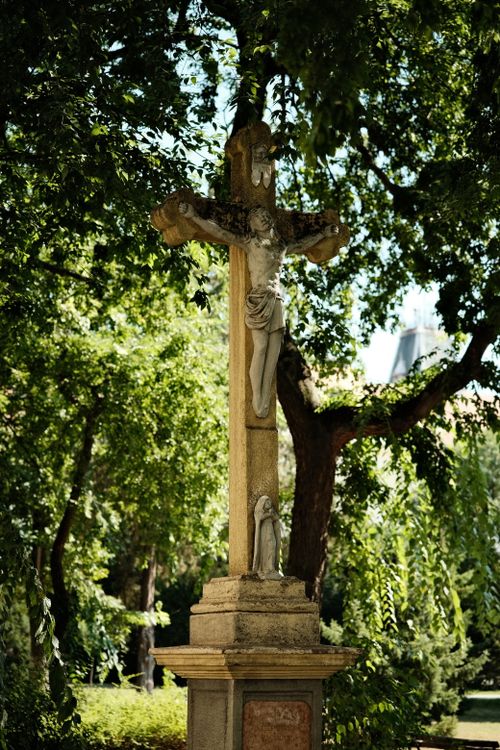 Free Stone cross with religious figure surrounded by lush trees in a peaceful park. Stock Photo