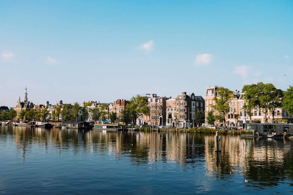 Beautiful aged houses located on shore of river in Amsterdam against cloudless blue sky