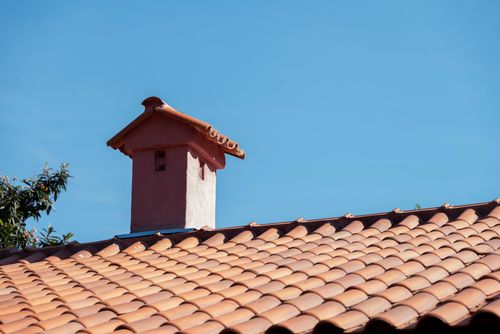 Free Close-up of a red tiled roof and chimney under a bright blue sky, showcasing vibrant architectural detail. Stock Photo