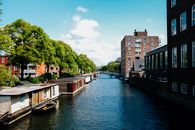 Picturesque channel in Amsterdam with traditional houseboats near modern buildings in city outskirts against blue sky