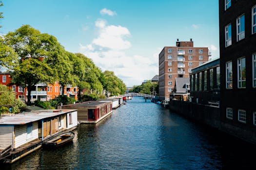 阿姆斯特丹风景如画的运河旁，传统的船屋与现代建筑相邻，映衬着蓝天