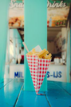 Crispy French fries served in a red gingham cone at an outdoor snack bar.