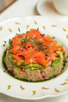 Delicious quinoa salad with smoked salmon, avocado, and herbs on a decorative plate.