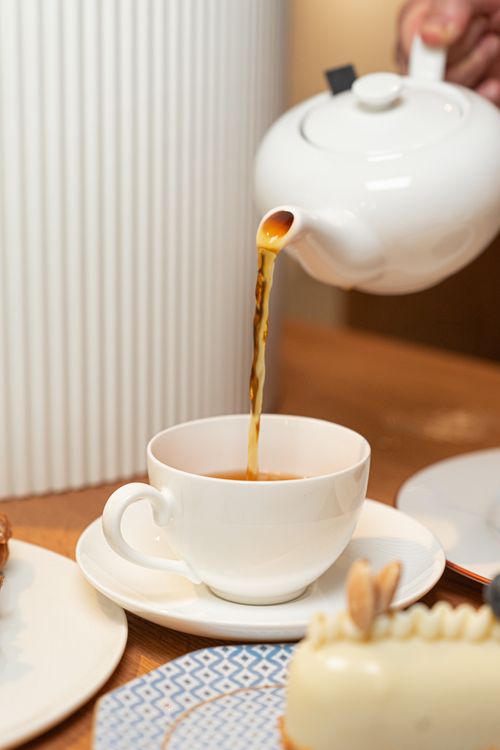 Free White teapot pouring tea into a teacup on a wooden table with desserts, capturing a serene tea time moment. Stock Photo