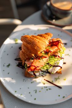 A close-up of a gourmet croissant sandwich with smoked salmon, avocado, and cream cheese, perfect for fine dining.
