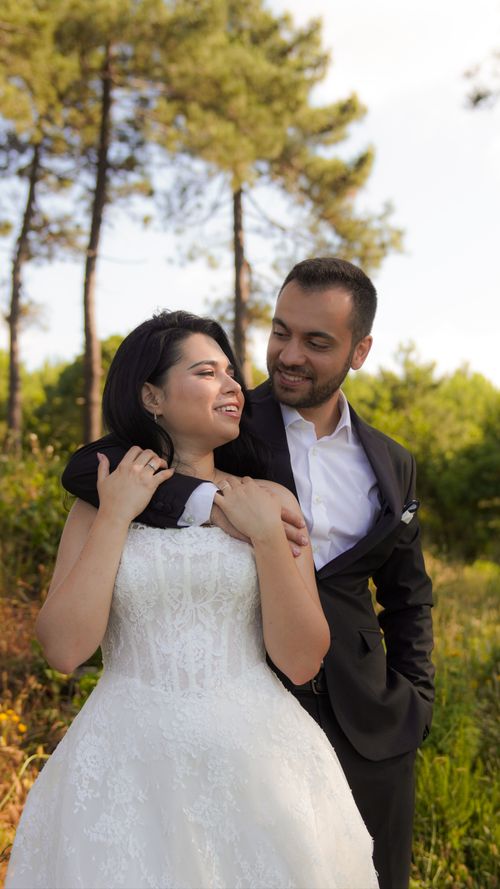 Free Bride in white gown and groom in black suit embracing outdoors with lush greenery. Stock Photo