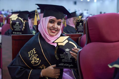 Free Young woman in cap and gown celebrating graduation with a smile, holding an award. Stock Photo