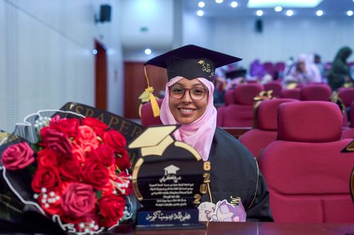Free A smiling graduate in cap and gown with flowers at the ceremony. Stock Photo