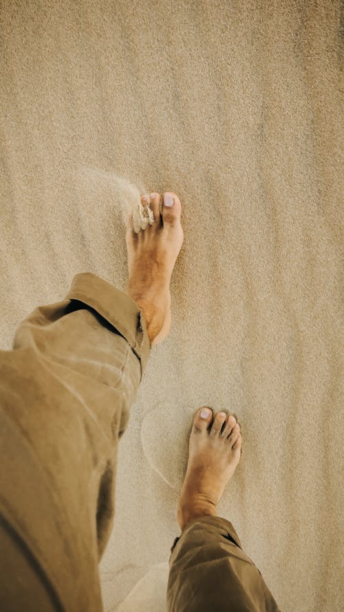From above of crop anonymous barefooted male traveler walking on sandy terrain in desert
