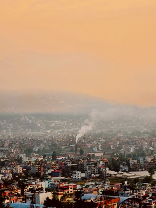 Free A panoramic view of a city with a smokestack emitting smoke at sunset. Stock Photo