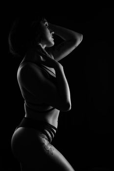Low-key monochrome portrait highlighting silhouette and tattoos in artistic style.