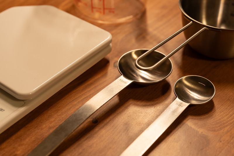 A close-up of kitchen utensils including a scale, measuring cups, and spoons on a wooden counter.