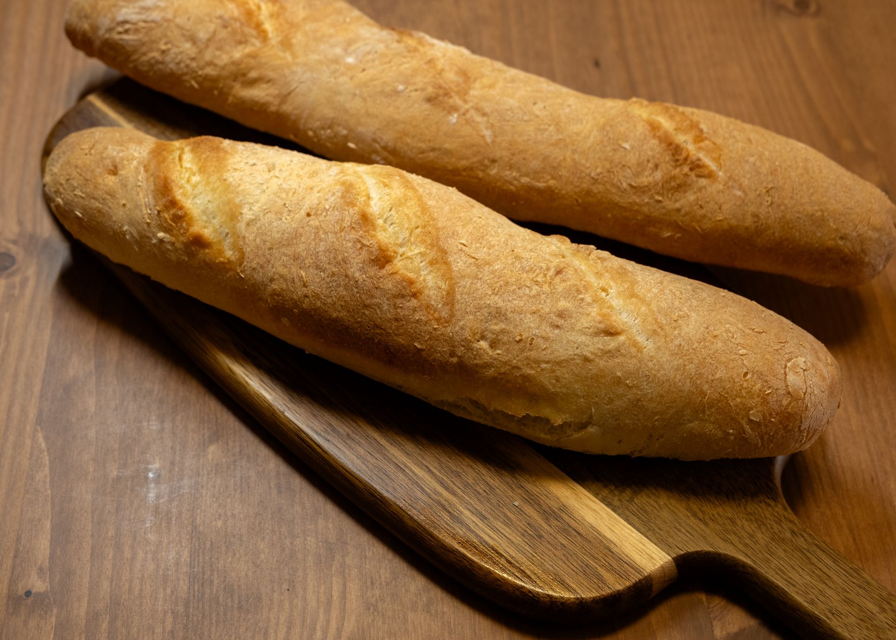 Two crusty baguettes resting on a wooden cutting board, showcasing their golden-brown texture.