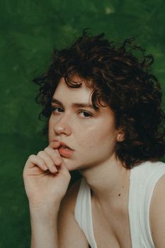 Close-up portrait of a young woman with curly hair, against a green backdrop, looking thoughtful.
