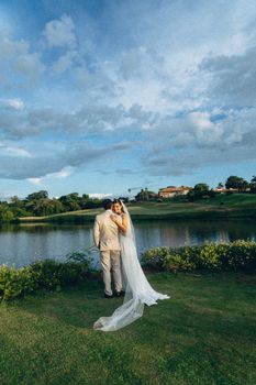 A bride and groom embrace outdoors by a lake in Maringá, Brazil. Perfect for wedding themes.