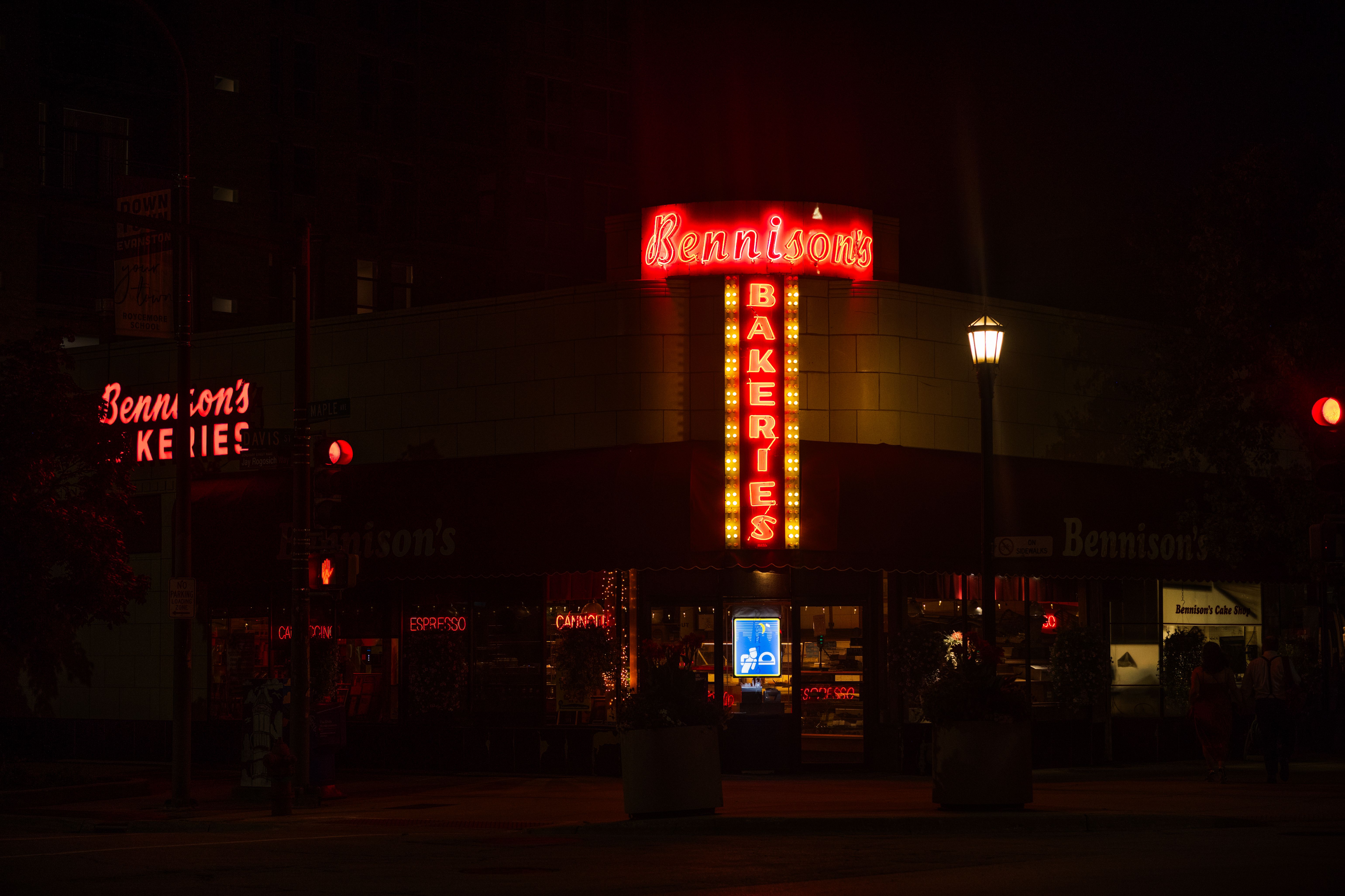 Illuminated neon sign of Bennison's Bakery at night on a dark urban street.