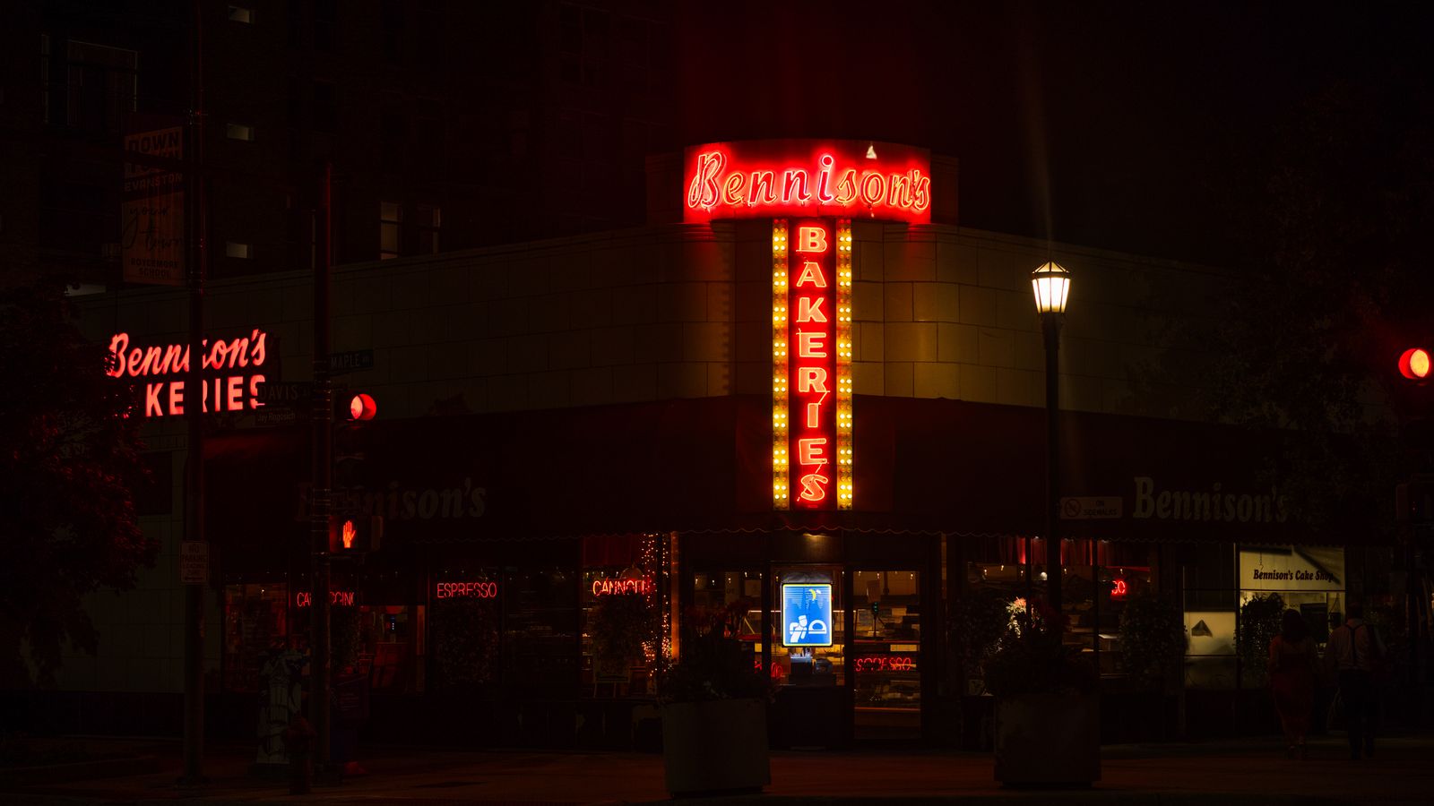Illuminated neon sign of Bennison's Bakery at night on a dark urban street.