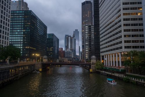 Free Skyline view of Chicago's skyscrapers along the river at dusk with a small boat passing under the bridge. Stock Photo